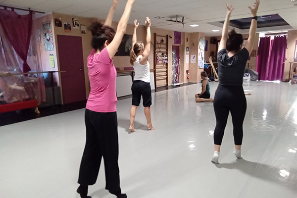 Cours de contemporain : 3 personnes étirent leurs bras vers le haut entraînant leur corps vers le haut également, 2 autres personnes sont au sol