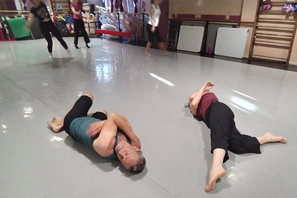 Cours de contemporain : 2 personnes sont en mouvement de torsion au sol, 3 autres personnes sont en mouvement debout en arrière plan